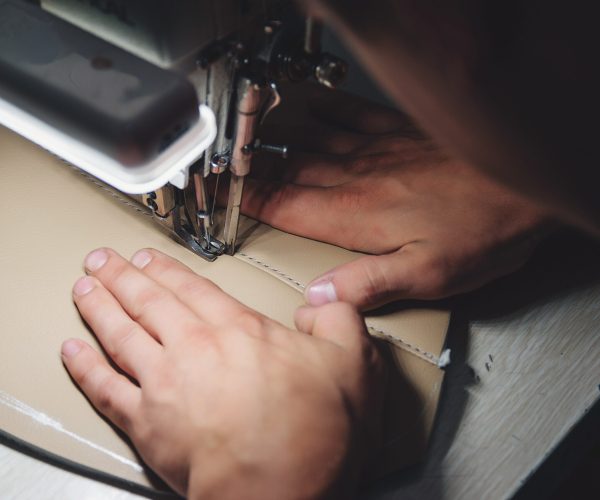 Working process of leather craftsman. Tanner sews leather on a special sewing machine, close up. Worker sewing leather product on the sewing machine. Leather worker workshop.
